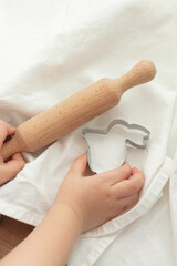 A child's hand holds an Easter steel rabbit-shaped mold. Home baked cookies for the holidays. Easter bunnies. Roll out the dough.