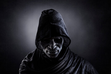 Fototapeta na wymiar Scary figure with hooded cape in the dark