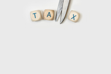 La palabra reducción de impuestos TAX escrita en cubos de madera junto a una tijera sobre un fondo gris claro. Vista superior. Copy space. Concepto de reducción, reducción o deducción de impuestos. - obrazy, fototapety, plakaty