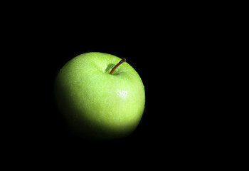 Green apple covered with water drops, black background. 