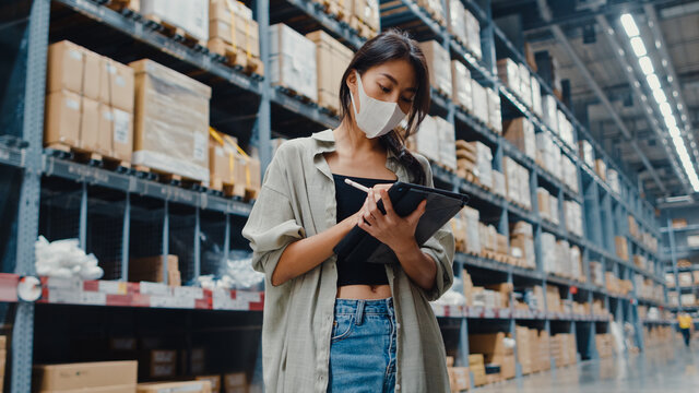 Young Asia Businesswoman Manager Wear Face Mask Looking For Goods Using Digital Tablet Checking Inventory Levels Stand In Retail Shopping Center. Distribution, Logistics, Packages Ready For Shipment.