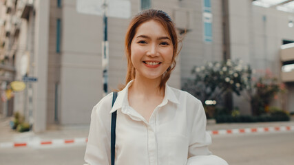 Successful young Asia businesswoman in fashion office clothes smiling and looking at camera while happy standing alone outdoors in urban modern city in the morning. Business on the go concept.