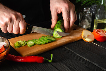 Chef cutting a green cucumber in kitchen in the restaurant. Making delicious salad with fresh vegetables