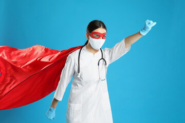 Doctor dressed as superhero posing on light blue background. Concept of medical workers fighting with COVID-19