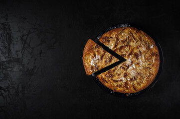 freshly baked homemade round shaped apple pie with sesame seeds on a plate with a cut piece on a black concrete background. top view. artistic moody photo with copy space for creative mockup