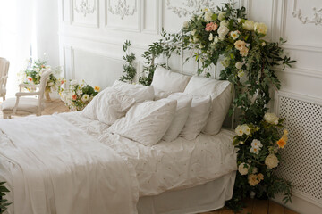 White bedroom. The bed is decorated with green leaves and flowers. Bed of newlyweds
