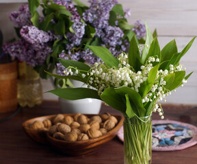 A bouquet of lilies of the valley and a bouquet of lilacs are on the table next to a bowl of nuts