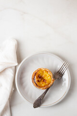 Pastel de Nata - portugese egg custard pies on white marble background. Portuguese pastie on ceramic plate with fork, top view