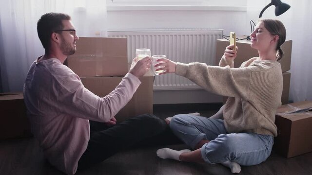 Happy couple relaxes after moving in a new home. Couple sits on floor and celebrates their moving in a new home. Woman drinks an alcohol and takes a photo of her husband