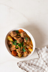 Goulash, beef stew with vegetables and thyme in a white plate with onion and greens.