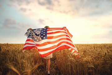 Back view of a girl in white dress wearing an American flag while running in a beautiful wheat field - Powered by Adobe