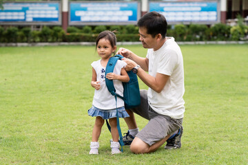 Asian father is helping to carry the schoolbag to daughter with happy moment after the school time,...