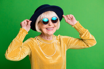 Photo of stylish old lady wear retro hat glasses yellow velvet shirt pearl necklace isolated green...