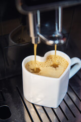 White cup in the form of a heart with coffee and a coffee machine