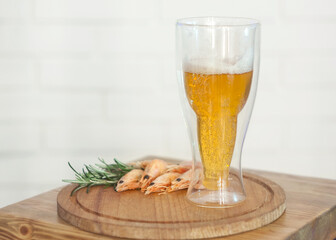 boiled shrimps are on the board, there is a glass of light foam beer in the shape of a bottle, a light background