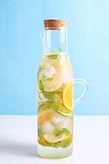 Classic lemon and orange lemonade with mint leaves in a pitcher. Virgin mojito, non alcoholic cocktail with ice in vintage bottle with handle and cork. Sky blue wall background. Copy space, close up.