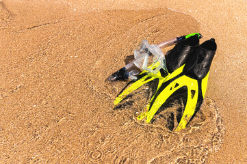Snorkel mask and flippers lie on the sandy beach next to the waves on a sunny day