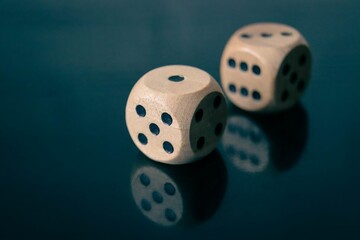 A close up of two wooden dice cubes on with a dark background and reflection. A concept for...