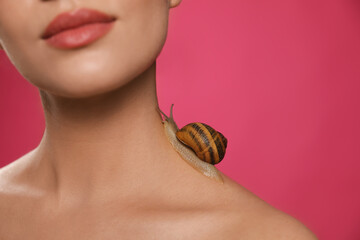 Beautiful young woman with snail on her neck against pink background, closeup