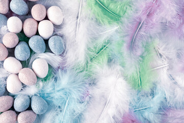 Happy Easter Holiday. Decorative Easter eggs on colorful feathers background. Copy space. Flat lay.