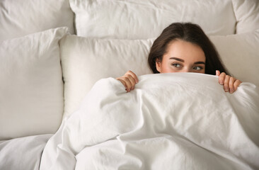Beautiful young woman wrapped with soft blanket relaxing in bed at home, above view