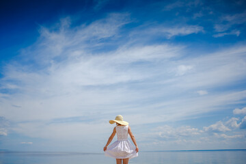 Fototapeta na wymiar Young woman in white dress and hat enjoy summer near the sea