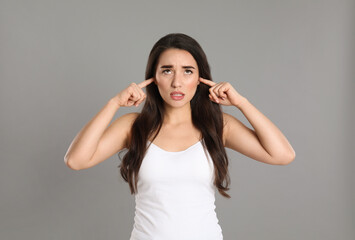 Fototapeta na wymiar Emotional young woman covering ears with fingers on grey background