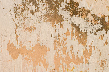 Grunge background of cracked peeling walls with peeled putty in beige tones.