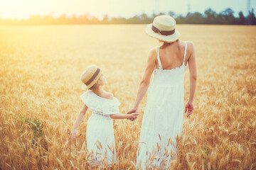 young mother and her daughter in white dress and straw hat at th