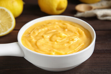 Delicious lemon curd in saucepan on dark wooden table, closeup