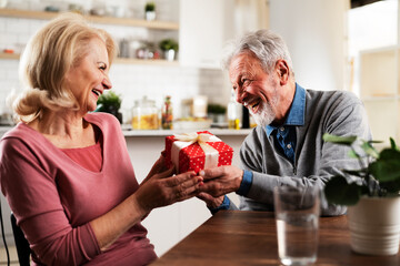 Husband giving a present to his wife. Senior man surprise his beautiful wife.