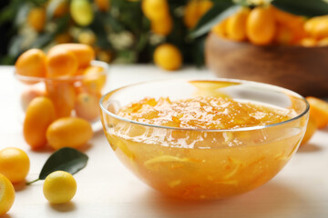 Delicious kumquat jam in bowl and fresh fruits on white wooden table