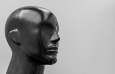 Mannequin made of black plastic. Mannequin head close-up, half-face view. Smooth contours without details. Glare.