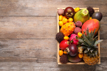 Crate with different exotic fruits on wooden table, top view. Space for text