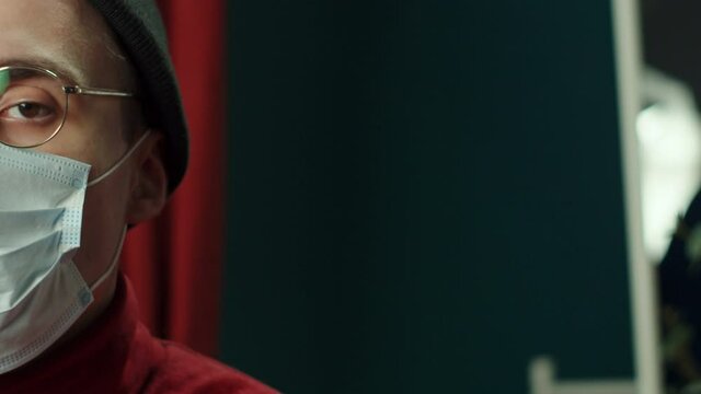 Half-face portrait of young man in protective mask, wearing glasses, hat. Headshot of funny hippster. Looking at the camera. Close-up of student. 