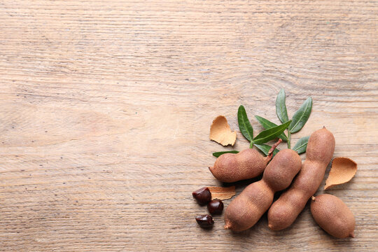 Ripe tamarinds and fresh leaves on wooden table, flat lay. Space for text