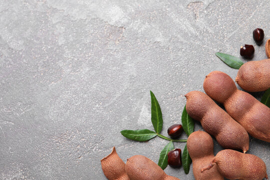 Ripe tamarinds and fresh leaves on grey table, flat lay. Space for text