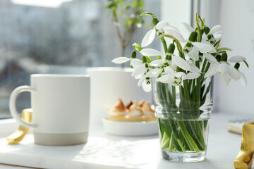 Beautiful snowdrops, cup of drink and dessert on white tray near window. Space for text