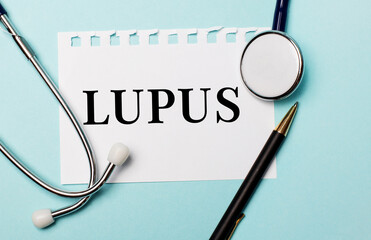 On a light blue background, a stethoscope, a pen and a sheet of paper with the inscription LUPUS....