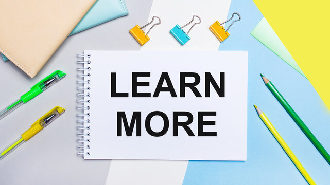 On a gray and blue background are stationery of yellow-green color, a notebook with the text LEARN MORE. Flat lay.