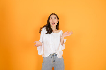 Portrait of pretty cute young asian girl with casual white shirt and jeans feeling excited, on orange background