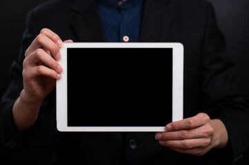 White tablet PC with blank screen in hands of man wearing black suit in black background