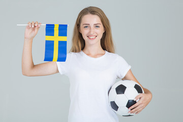 Beautiful young woman with the flag of Sweden and a soccer ball in her hands, looking at the...