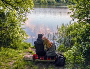 Couple sitting together on a log looking on the calm river in springtime