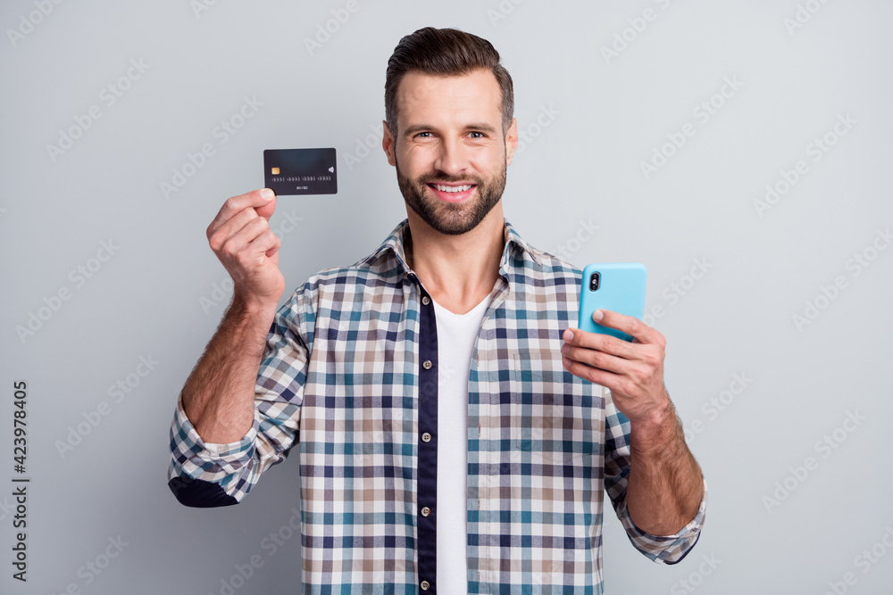 Poster Photo portrait of cheerful man keeping mobile phone showing bank credit card isolated on grey color background