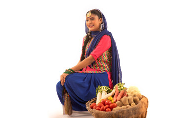 A woman in a Giddha costume sitting with a vegetable basket by her side.	