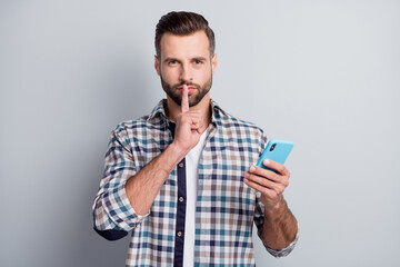 Portrait of mysterious attractive bearded guy using gadget showing shh sign isolated over gray pastel color background