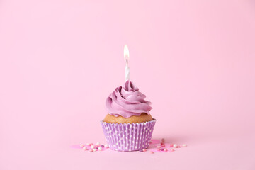 Delicious birthday cupcake with burning candle and sprinkles on pink background