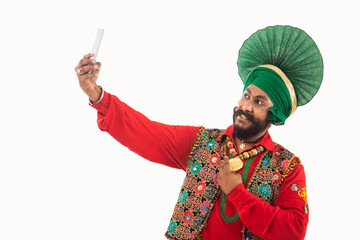  A man in Bhangra Costume taking a selfie in his phone.	