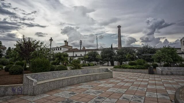 Timelapse forming clouds over a century-old fireplace in a square with people passing by. Graffiti on a stone bank